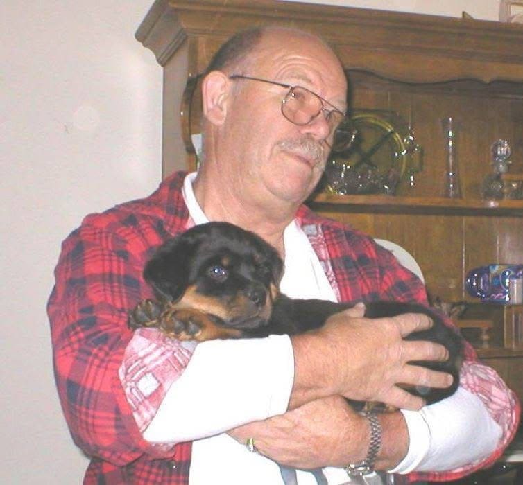 Man in red shirt holding Rottweiler puppy.