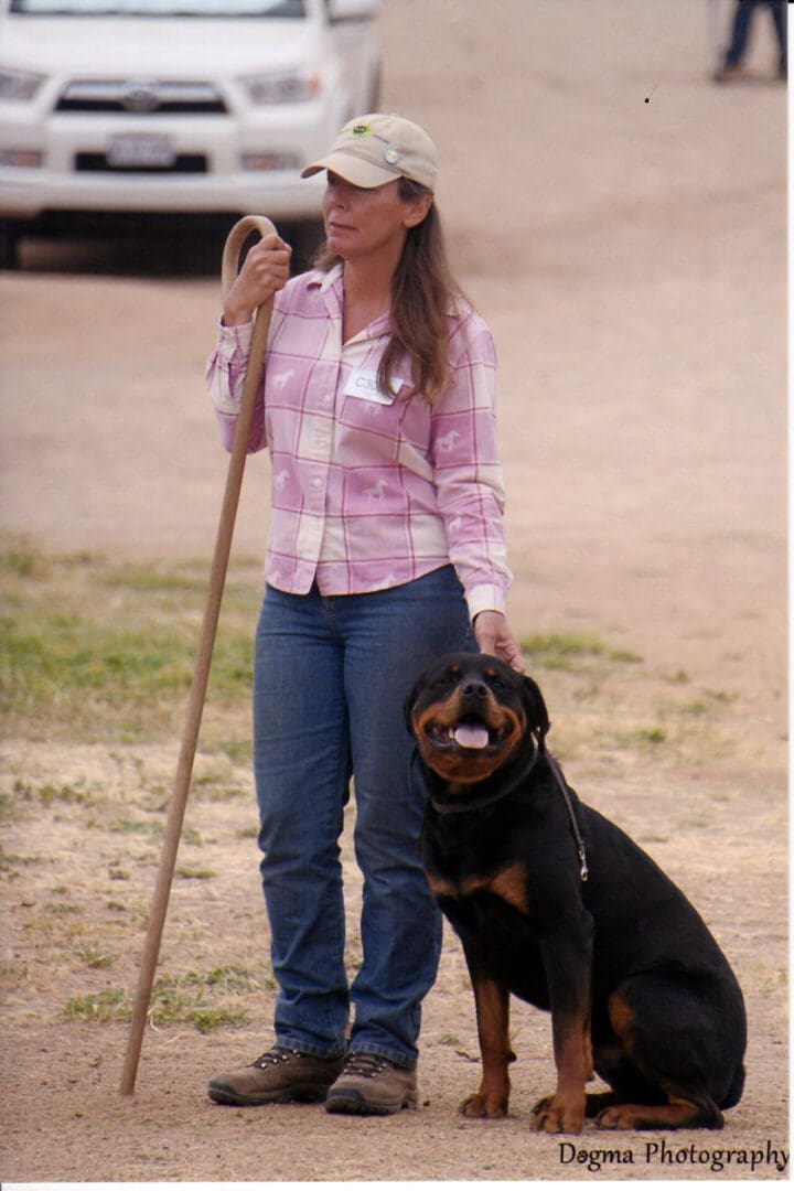 Woman with dog and walking stick outdoors.